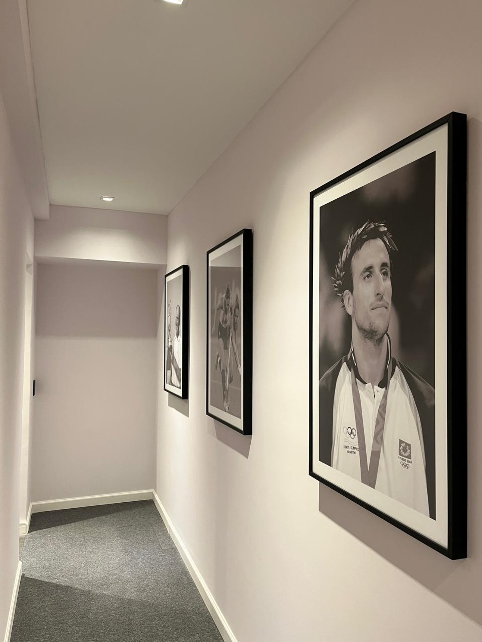 Pasillo moderno con retratos en blanco y negro de atletas — proyecto Oficinas Cordoba, por Arcucci Arquitectura, en Av. Córdoba